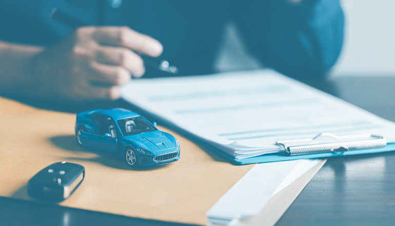 hombre revisando los cambios en su seguro de coche que afectan al cobro de su indemnizacion, con un coche y unas llaves de coche al lado de los papeles